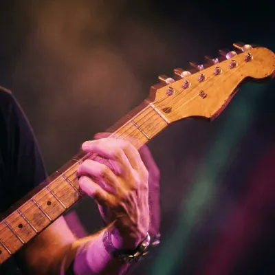 Close-up of a hand playing an electric guitar neck under stage lights