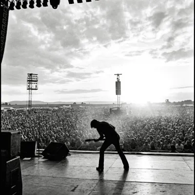 Silhouetted guitarist performing for a crowd at an outdoor music festival
