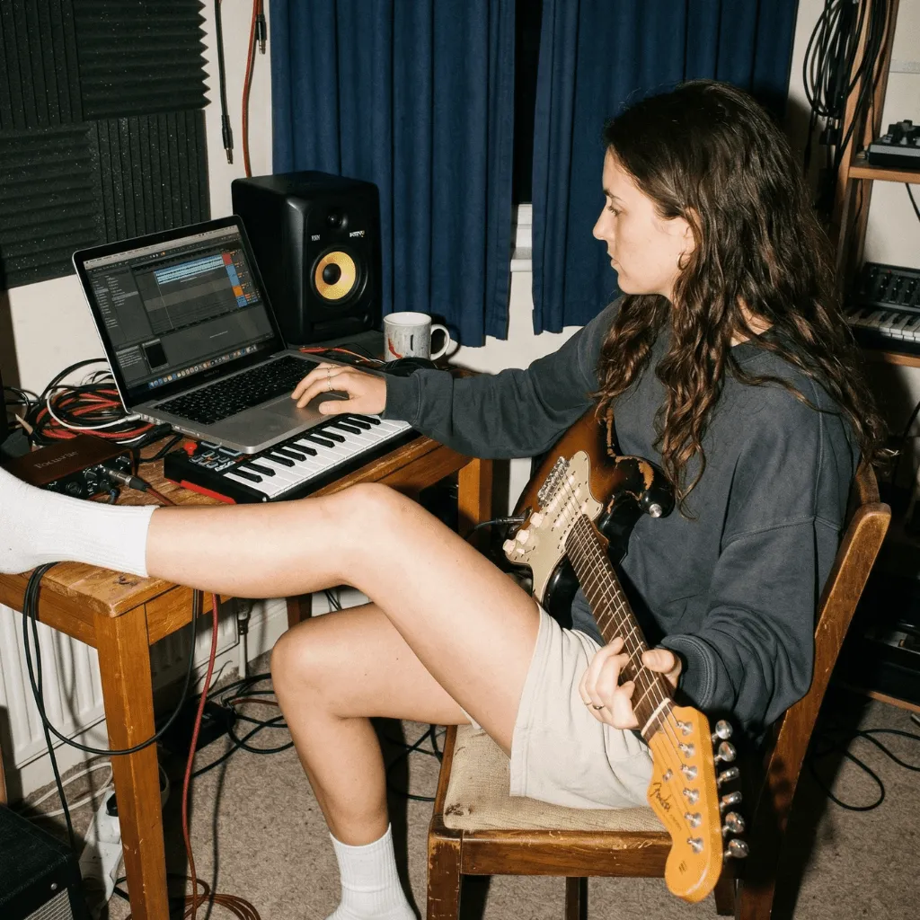 A musician playing guitar in a home studio with recording gear